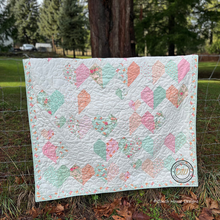 Kind Hearts lap quilt with large heart shaped heart pattern on a cream background draped over a country fence.
